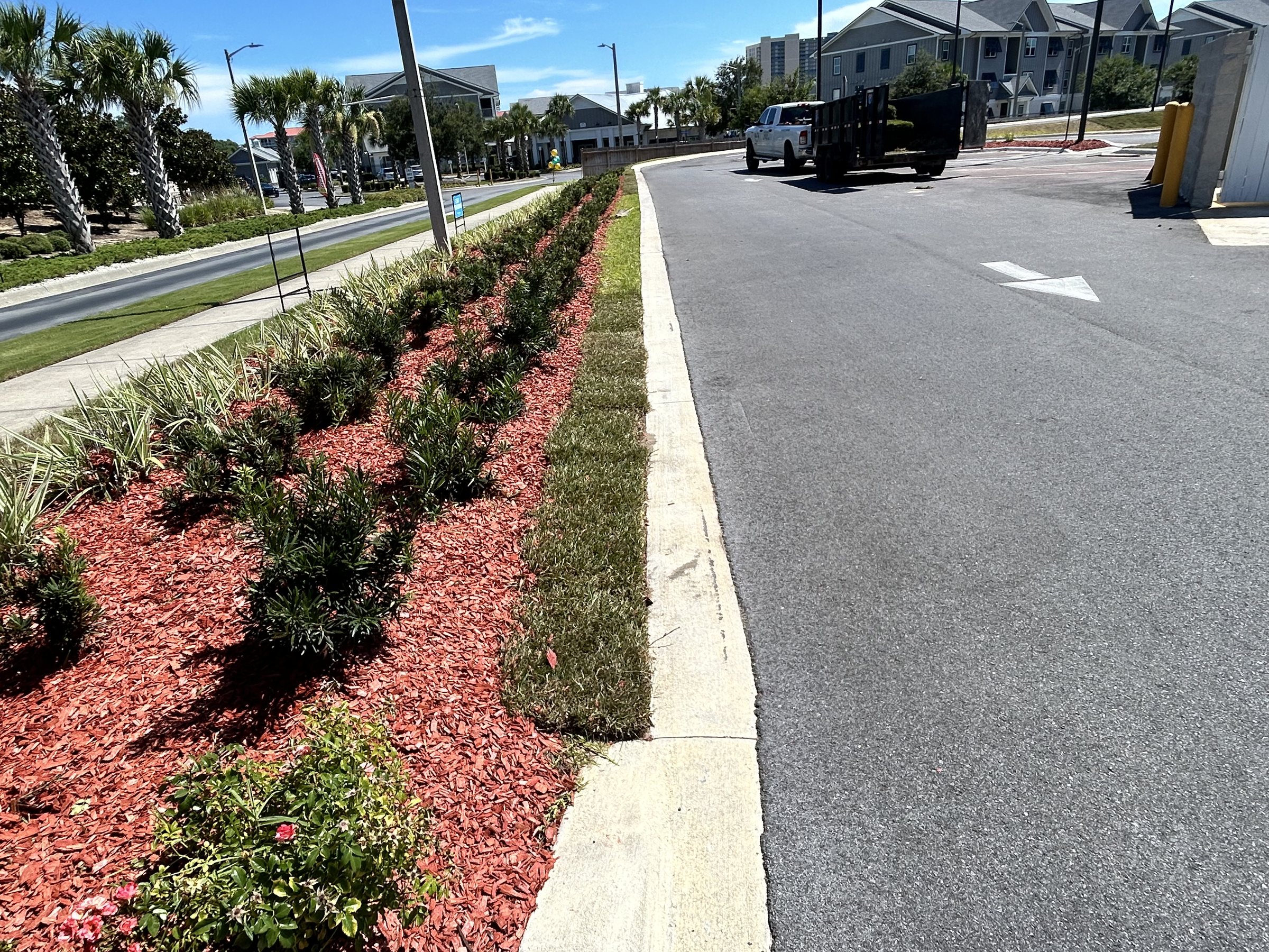 Long mulched planting bed and fresh sod edge along a commercial drive, with an R&B Landscape truck on site