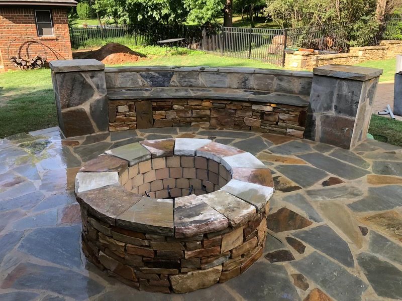 Round stone fire pit with a curved stone seating wall on a flagstone patio