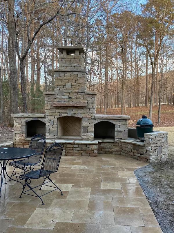 Stone outdoor fireplace on a travertine patio with wrought iron bistro seating