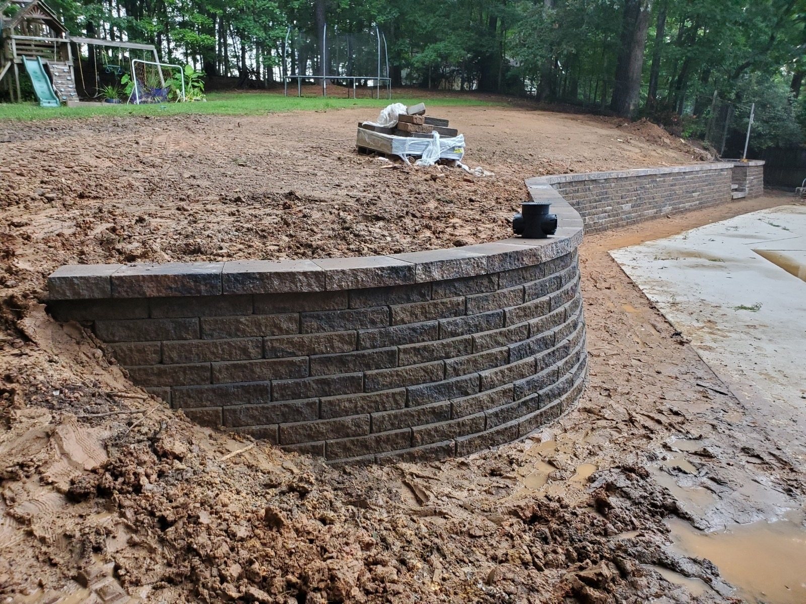 Curved segmental block retaining wall under construction with freshly graded soil