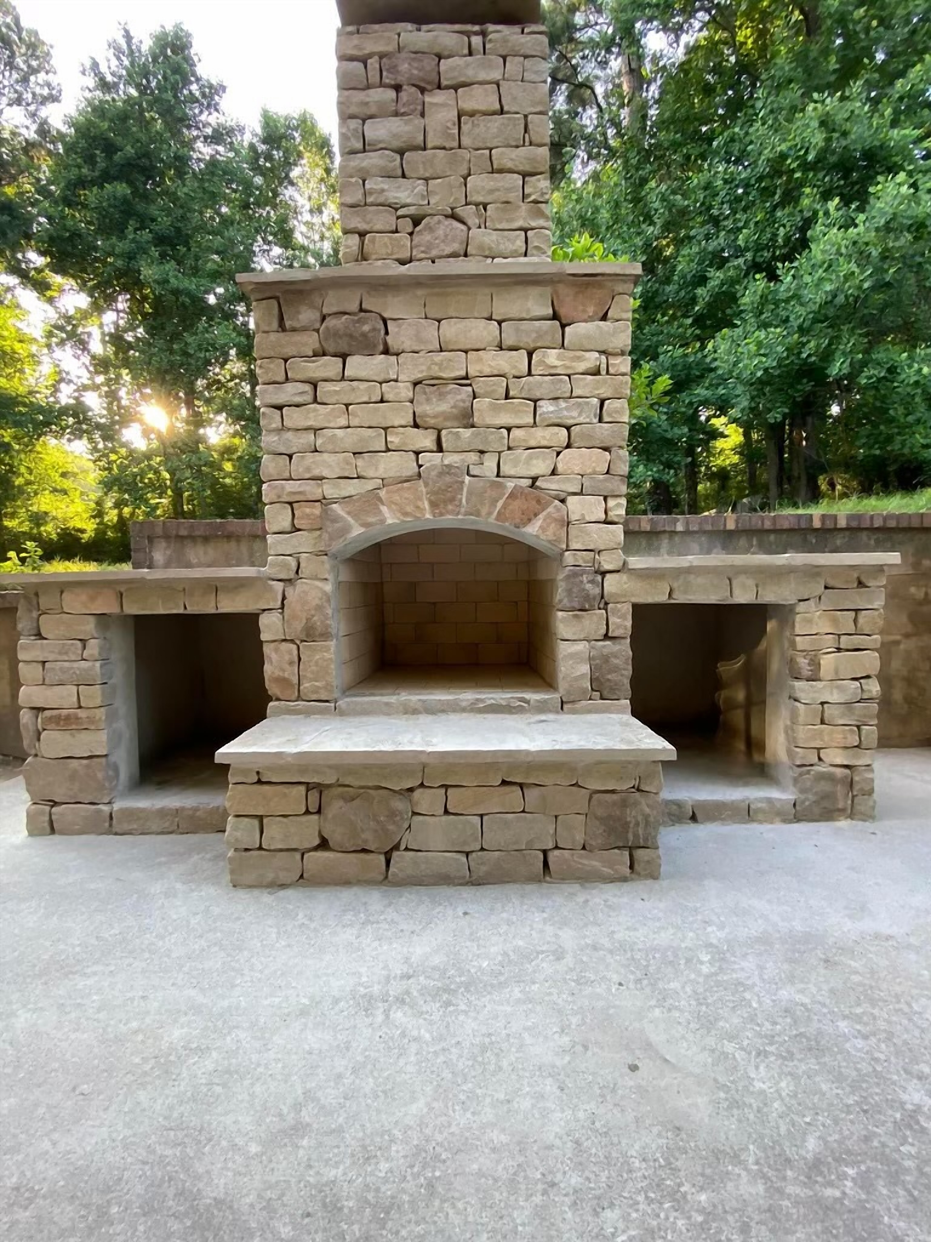 Custom stone outdoor fireplace with built-in wood storage niches, lit at dusk