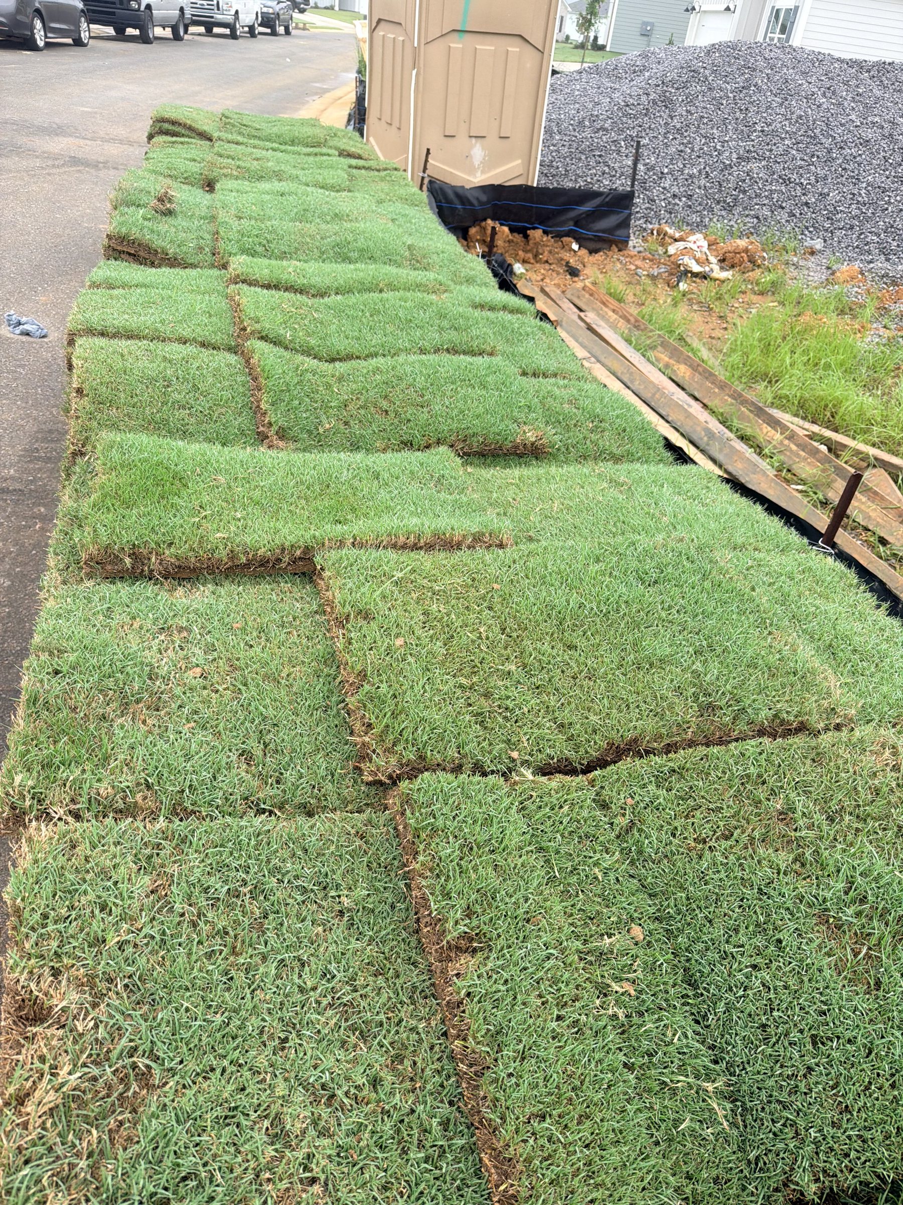Pallets of cut sod staged along a driveway on a new-construction lot, ready for installation